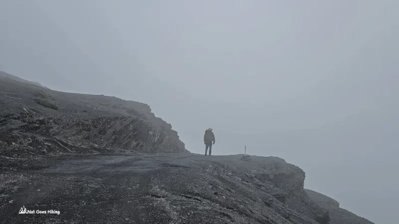 Hiker standing on a rocky ledge near a drop-off in heavy fog at Abra Chucura pass on the El Choro Trek