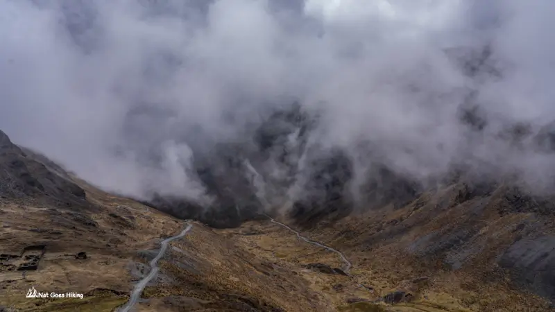 Narrow road winding through a cloud-filled Andean valley with clouds rolling over the ridges on the El Choro Trek