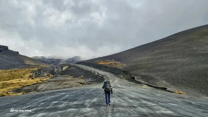 Hiker with a backpack walking a gravel road into fog at the start of El Choro Trek