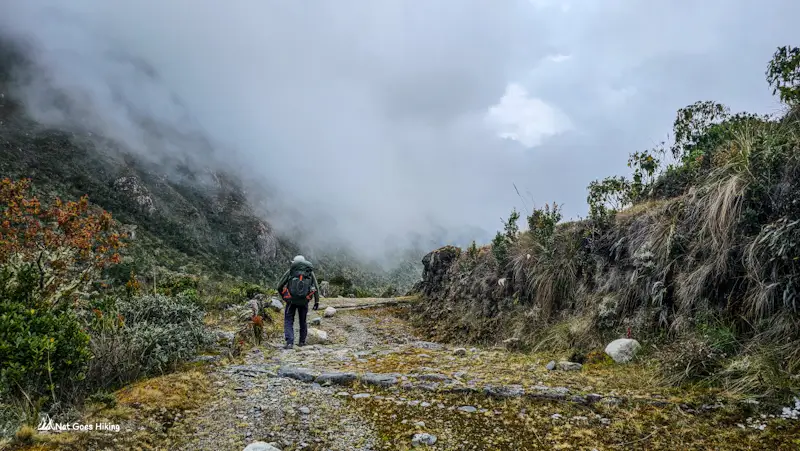 Hiker with a backpack on a stone-paved section of the Camino del Choro with mist over the slopes